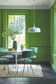 Chairs upholstered in Crémaillère indoor printed fabric in Green by Raoul Dufy sat around a white modern table in room with bright green walls. Design by Little Greene